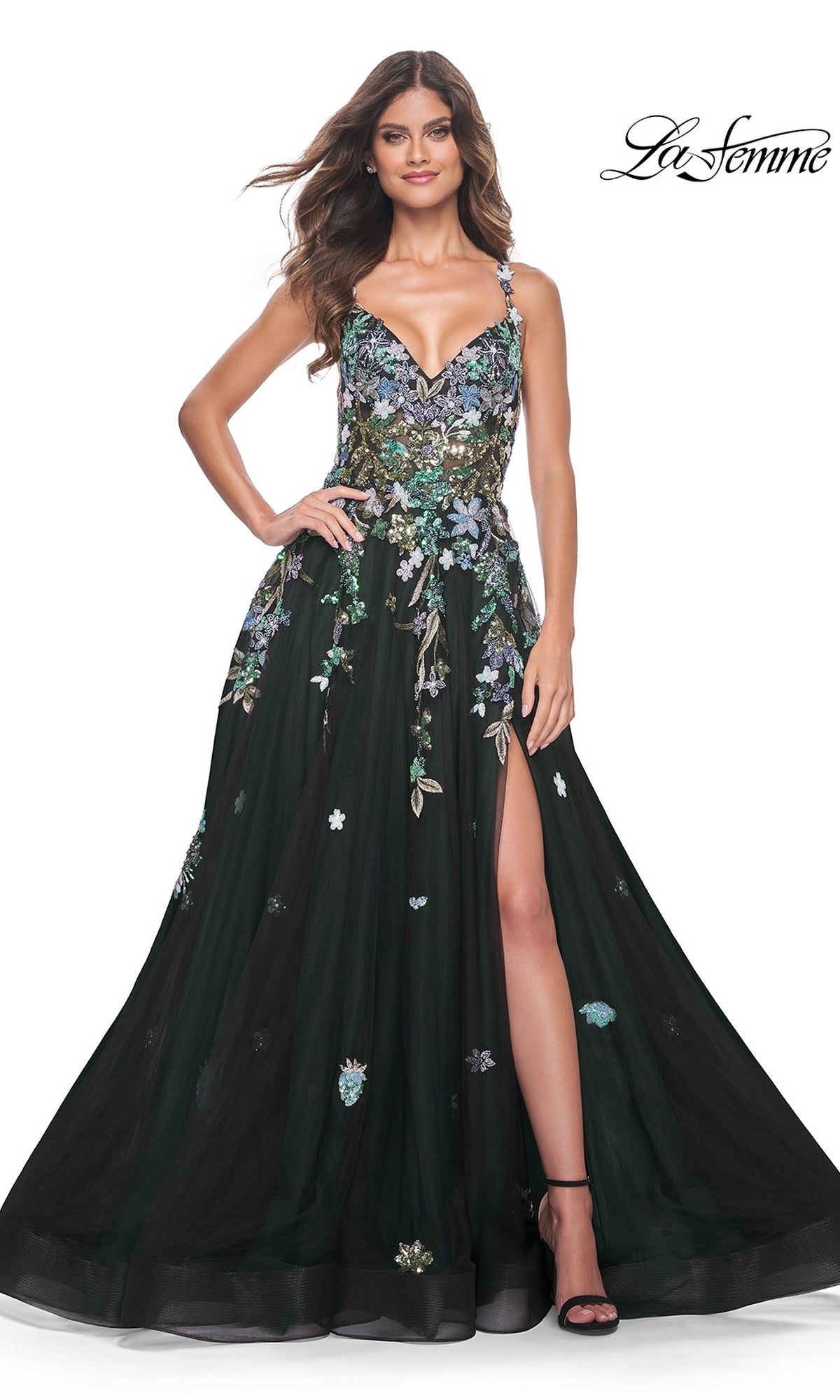 A woman poses with one hand on her hip, wearing the La Femme Sequin Flower-Print Long Prom Dress 32023—black, long A-line design featuring sequin flower embroidery, thin straps, and a thigh-high slit. The 