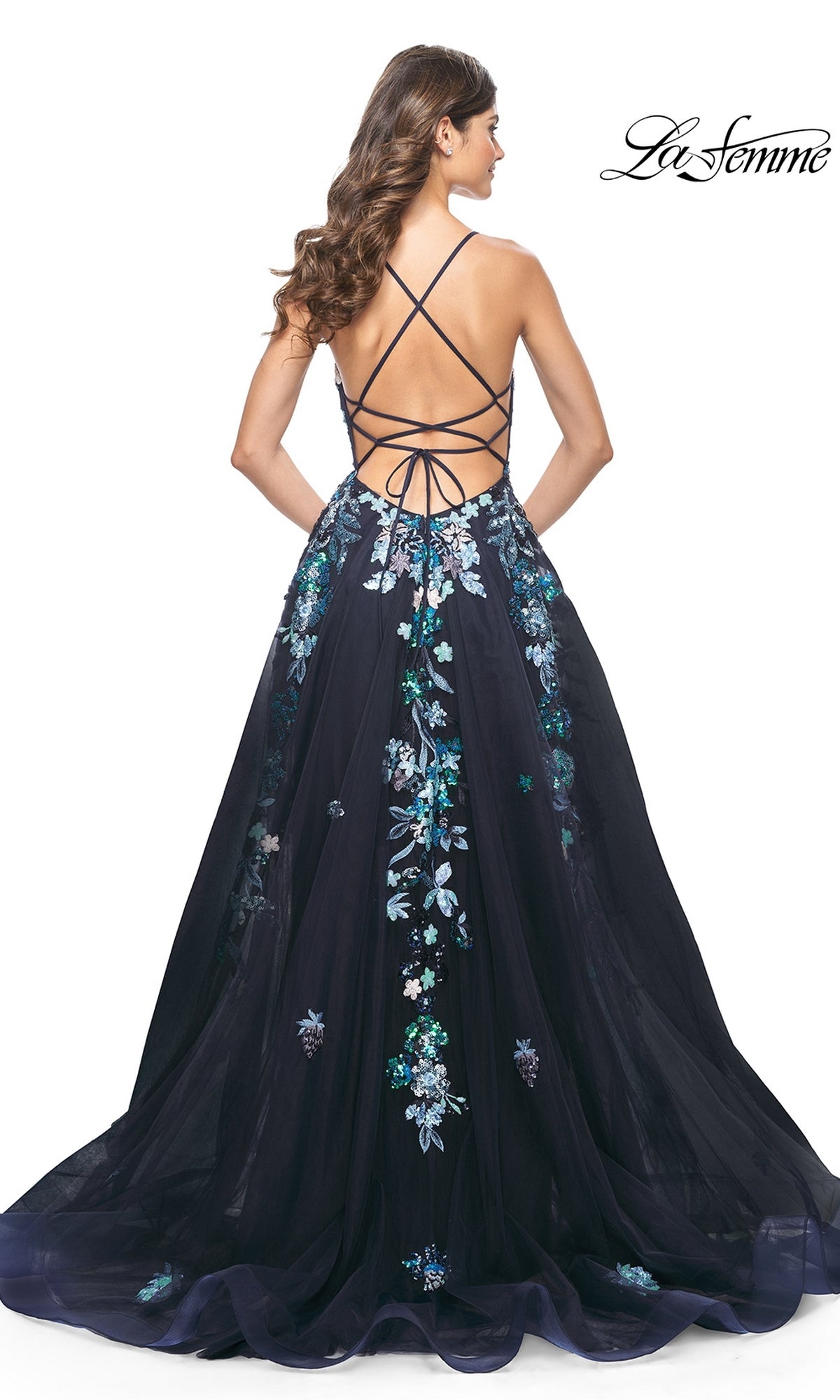 A woman with loose waves stands facing away in the La Femme Sequin Flower-Print Long Prom Dress 32023, featuring navy blue sequin floral embroidery and an open strappy back.