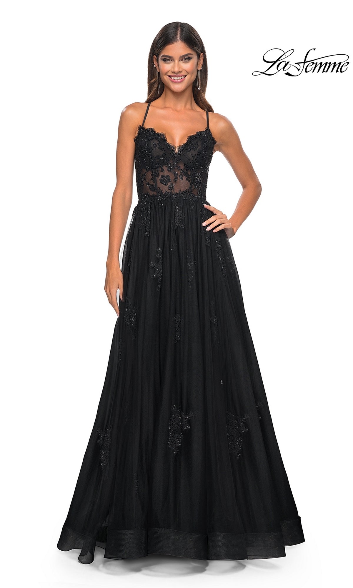 Woman wearing the La Femme Sheer-Corset Long A-Line Prom Dress 32028, a black floor-length embroidered lace gown with spaghetti straps, standing and smiling against a white background. 