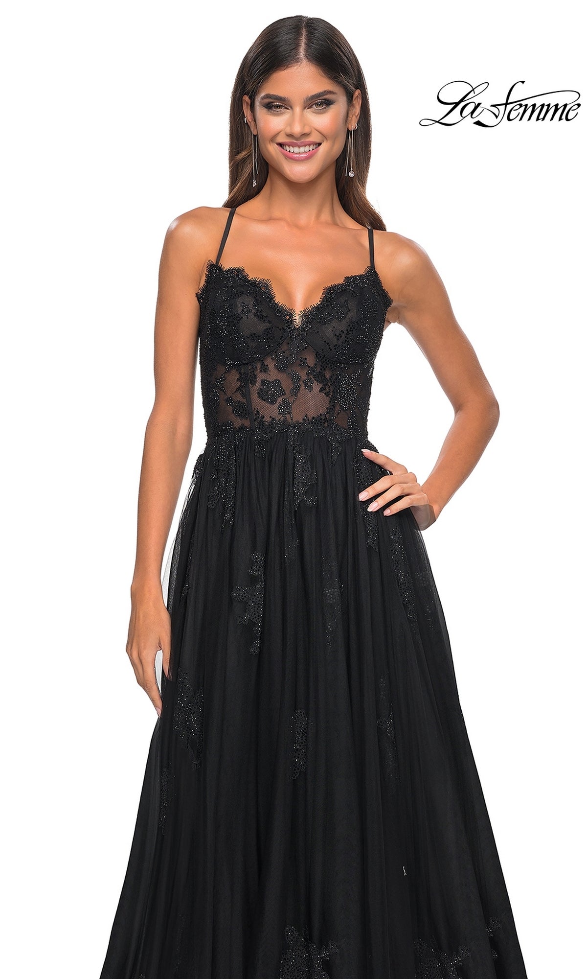 A woman stands smiling against a white background, wearing the La Femme Sheer-Corset Long A-Line Prom Dress 32028—sleeveless with black embroidered lace, a sheer bodice, and floral detailing. 
