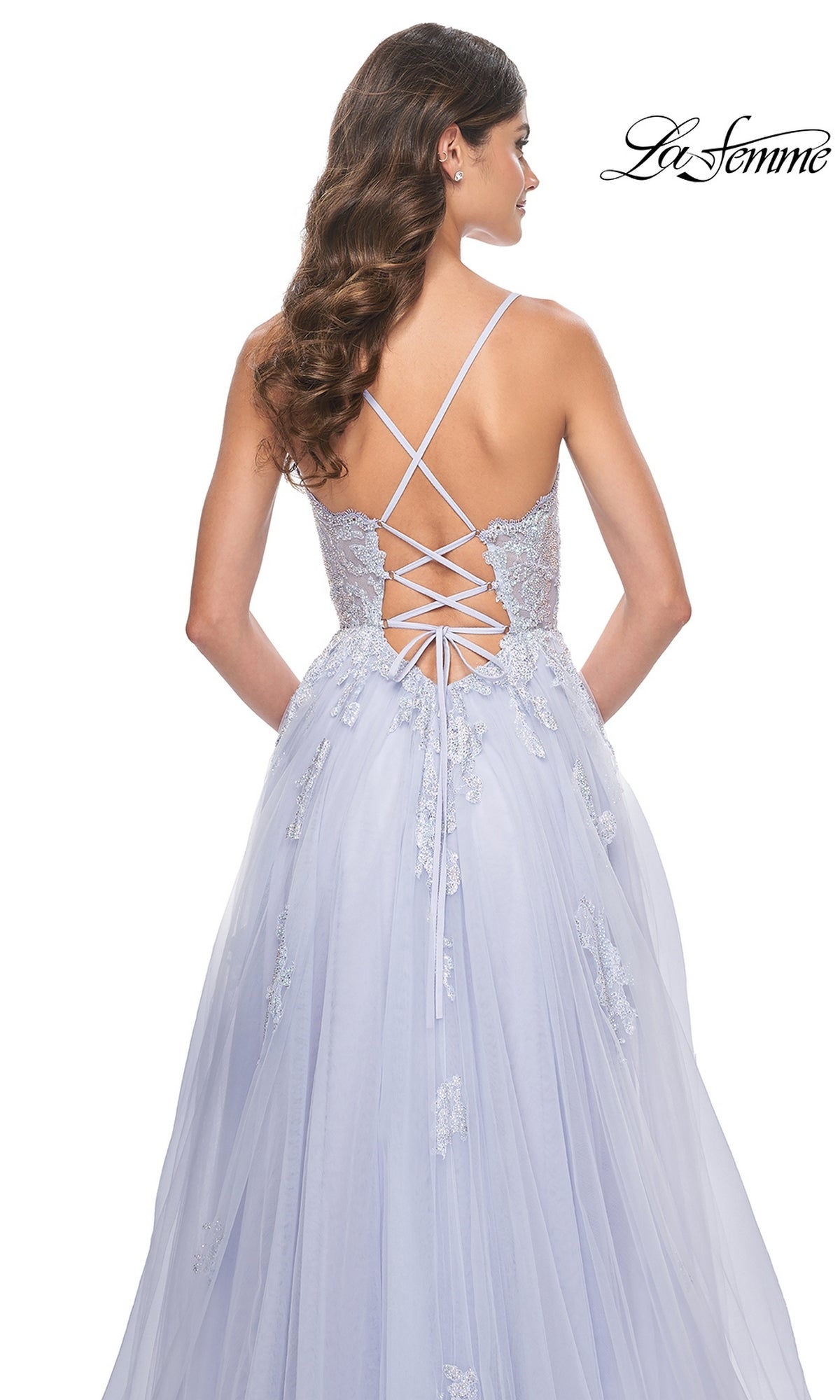 A woman models the La Femme Sheer-Corset Long A-Line Prom Dress 32028, featuring embroidered floral appliqué, thin straps, and a light blue lace-up back, standing against a white background.