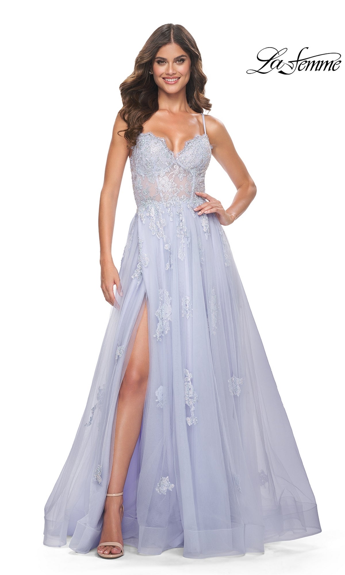 A woman wears the La Femme Sheer-Corset Long A-Line Prom Dress 32028 in light lavender with thin straps, a sheer bodice, floor-length A-line silhouette, leg slit, and embroidered lace. The La Femme logo appears in the top right corner.