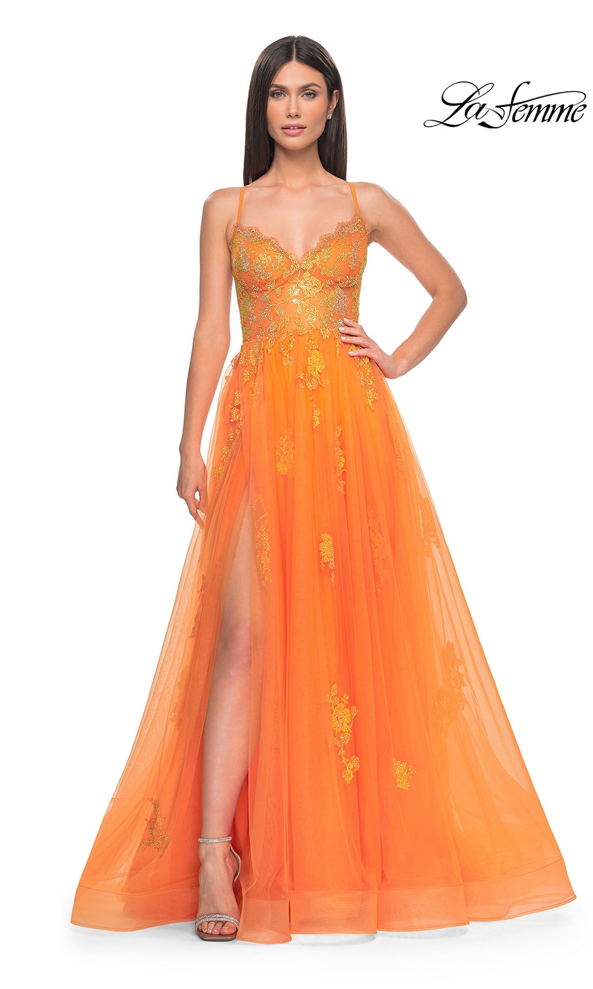 A woman stands against a white background wearing the La Femme Sheer-Corset Long A-Line Prom Dress 32028, featuring orange embroidered lace, gold floral details, a thigh-high slit, and spaghetti straps.