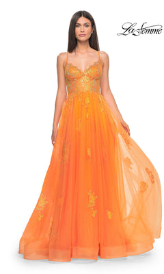 A woman wears the La Femme Sheer-Corset Long A-Line Prom Dress 32028, featuring orange tulle, gold floral embroidery, and thin straps, standing against a white background.