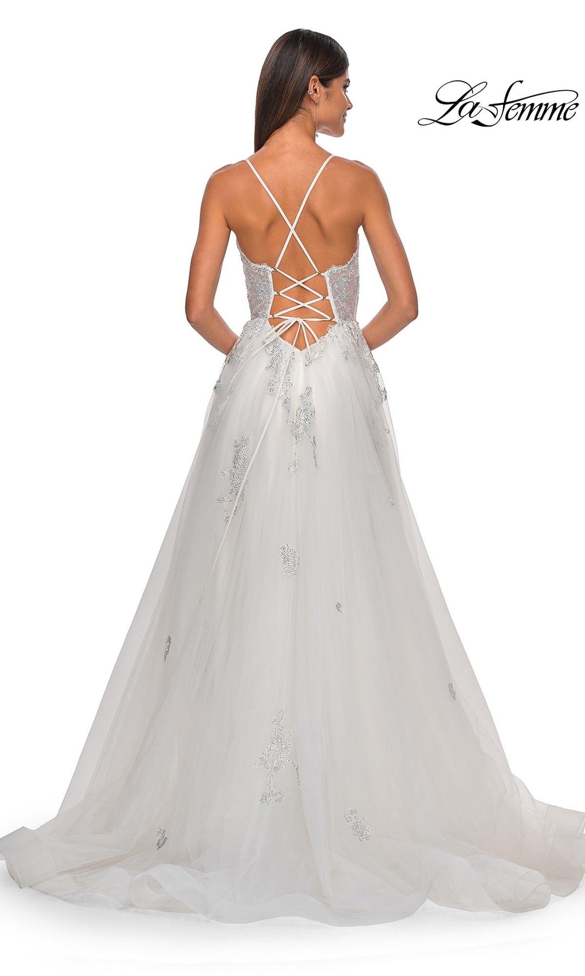 A woman faces away in the La Femme Sheer-Corset Long A-Line Prom Dress 32028, a white gown with thin crisscross straps, lace-up open back, long embellished tulle skirt, and elegant sheer corset detail.