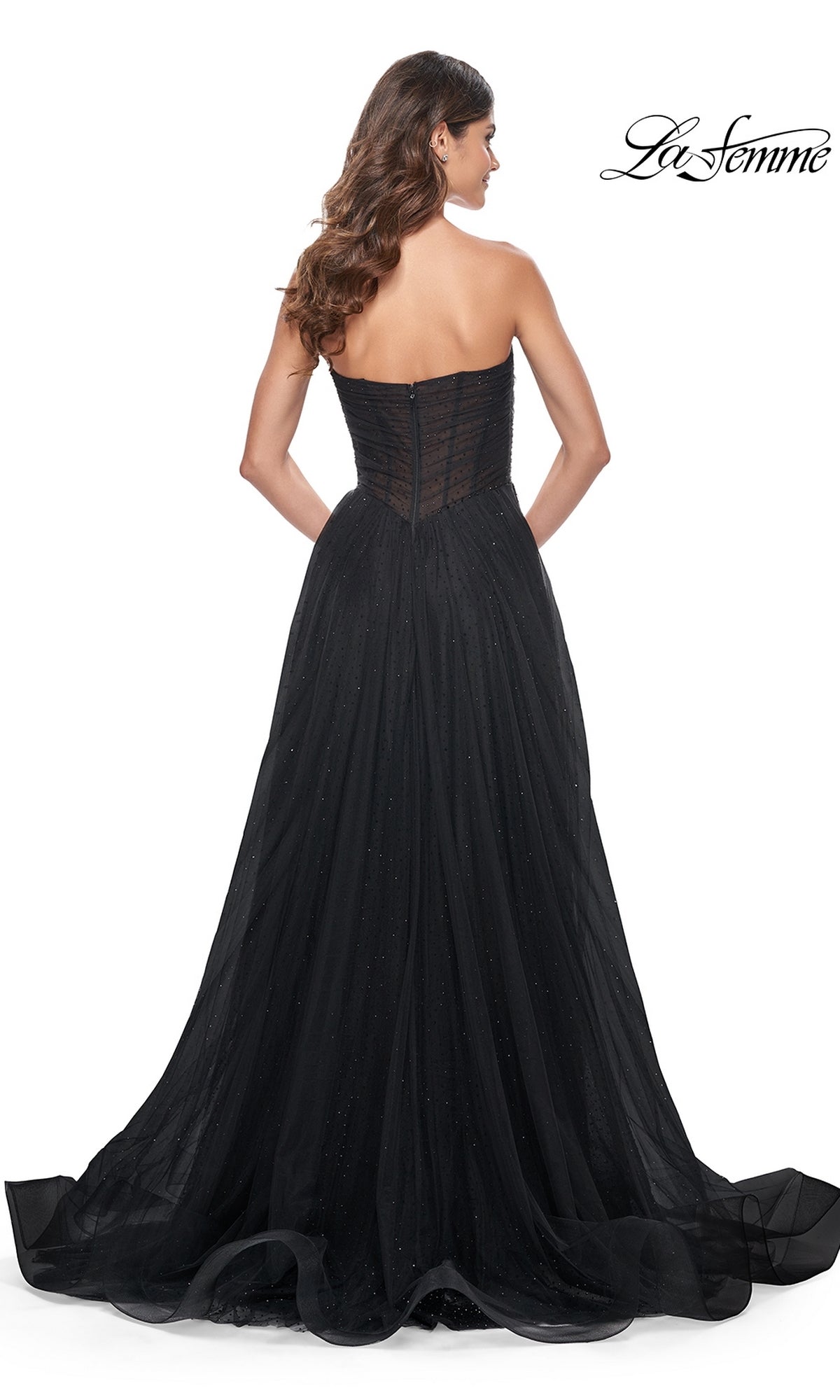 A woman is shown from the back wearing the La Femme Long Black Strapless Prom Ball Gown 32029, featuring a fitted bodice, flowing floor-length tulle skirt, and subtle sparkling details against a white background.