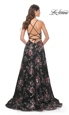 A woman stands facing away in the La Femme Floral-Sequin Long A-Line Prom Dress 32031, a black gown adorned with pink and purple floral sequins and an open crisscross back for an elegant prom look.