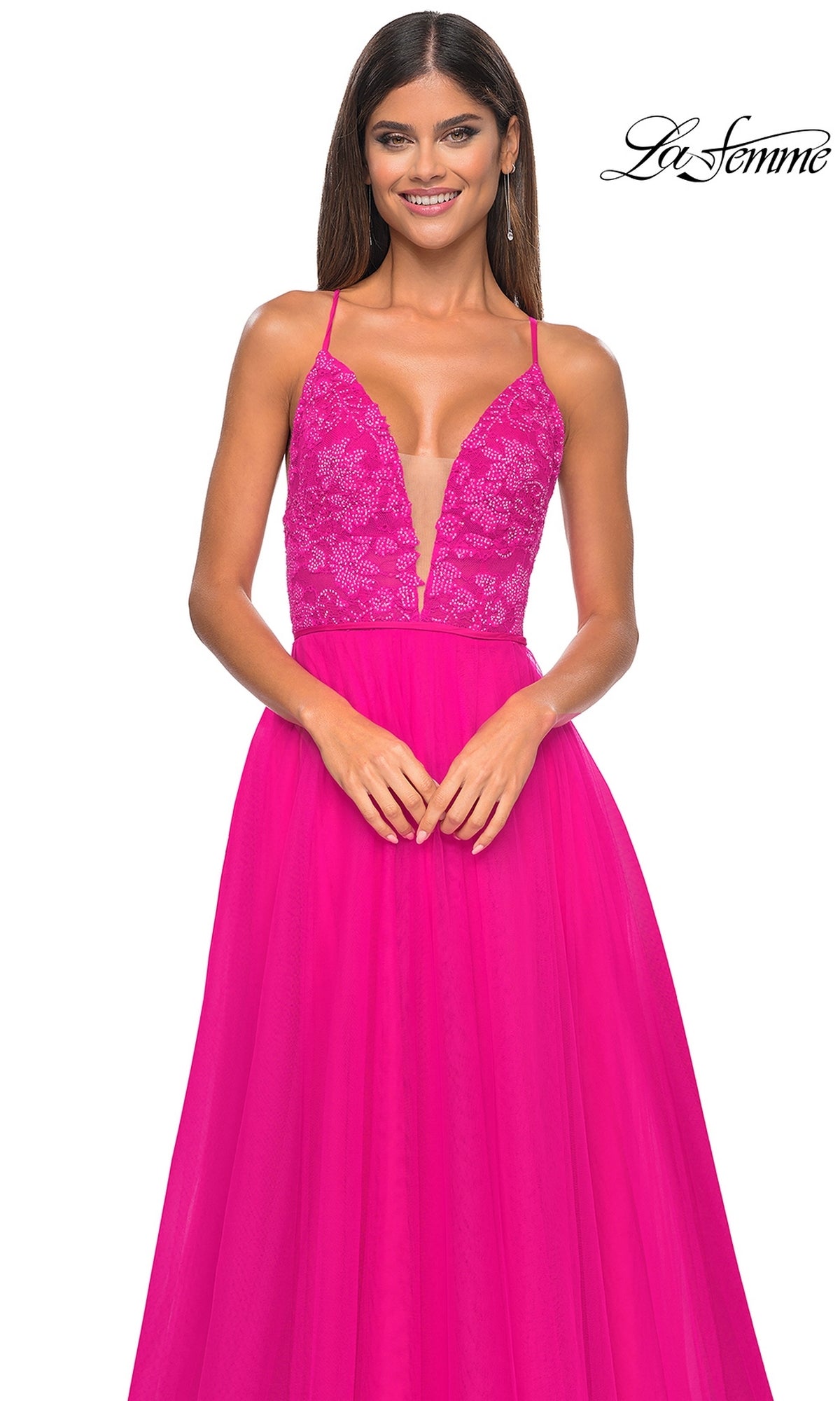 A woman models the La Femme Deep V-Neck Long Tulle Prom Gown 32059 in bright pink, featuring a lace bodice and flowing long tulle skirt, standing against a white background.