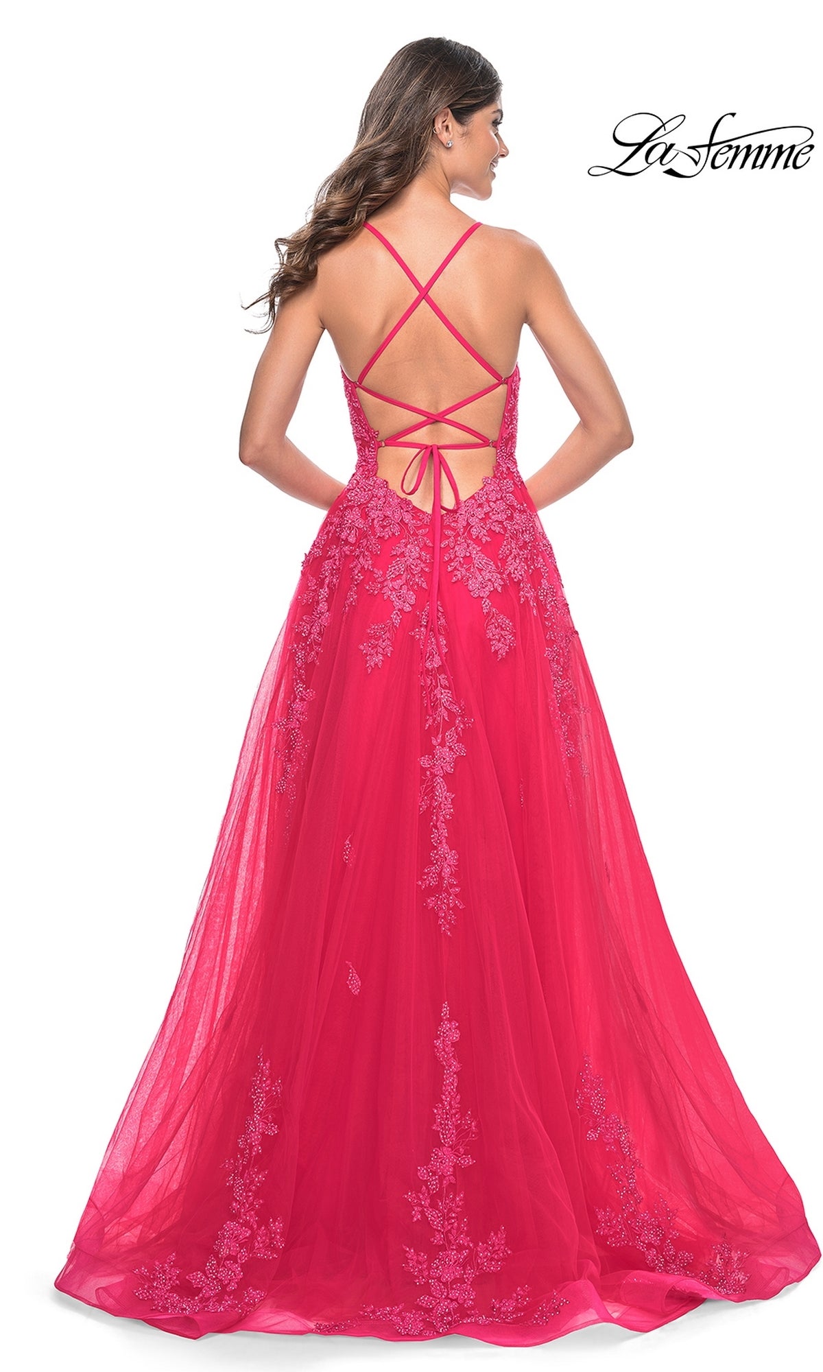 A woman faces away from the camera in the La Femme Embroidered-Lace Long Prom Dress 32062, a sleeveless, floor-length pink gown featuring embroidered lace, an open back, and crisscross straps.