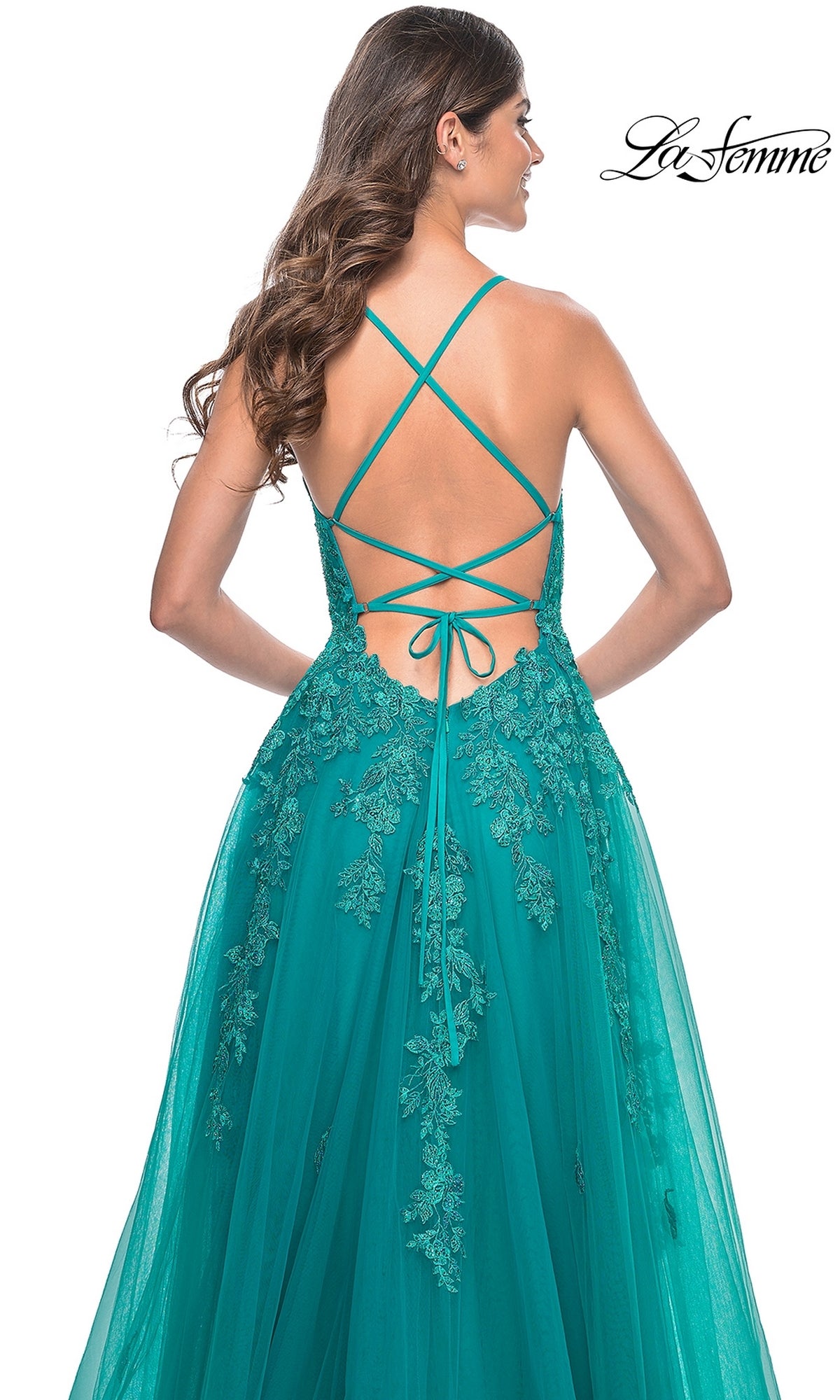 A woman stands with her back to the camera, wearing the teal La Femme Embroidered-Lace Long Prom Dress 32062, featuring a crisscross open back and floral lace details.