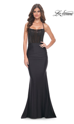 A woman models the La Femme Long Black Corset Prom Dress 32064, showcasing its fitted bodice, sheer corset detail, and floor-length skirt against a white background.
