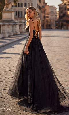 A woman in a black La Femme Long Sweetheart Prom Ball Gown 32065 with an open back stands on a cobblestone street, surrounded by historic city buildings.