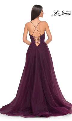 A woman in the La Femme Long Sweetheart Prom Ball Gown 32065, featuring a deep purple hue, lace-up open back, thin straps, and a flowing tulle overlay skirt, is shown elegantly from behind.