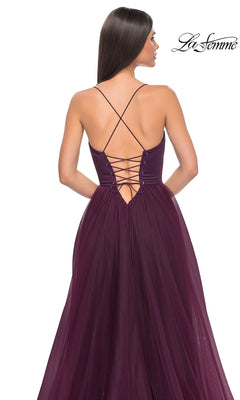 A woman wears the La Femme Long Sweetheart Prom Ball Gown 32065 in deep purple, featuring a sleeveless design, lace-up open back with crisscross straps, and a floor-length tulle skirt. "La Femme" is seen in the corner.