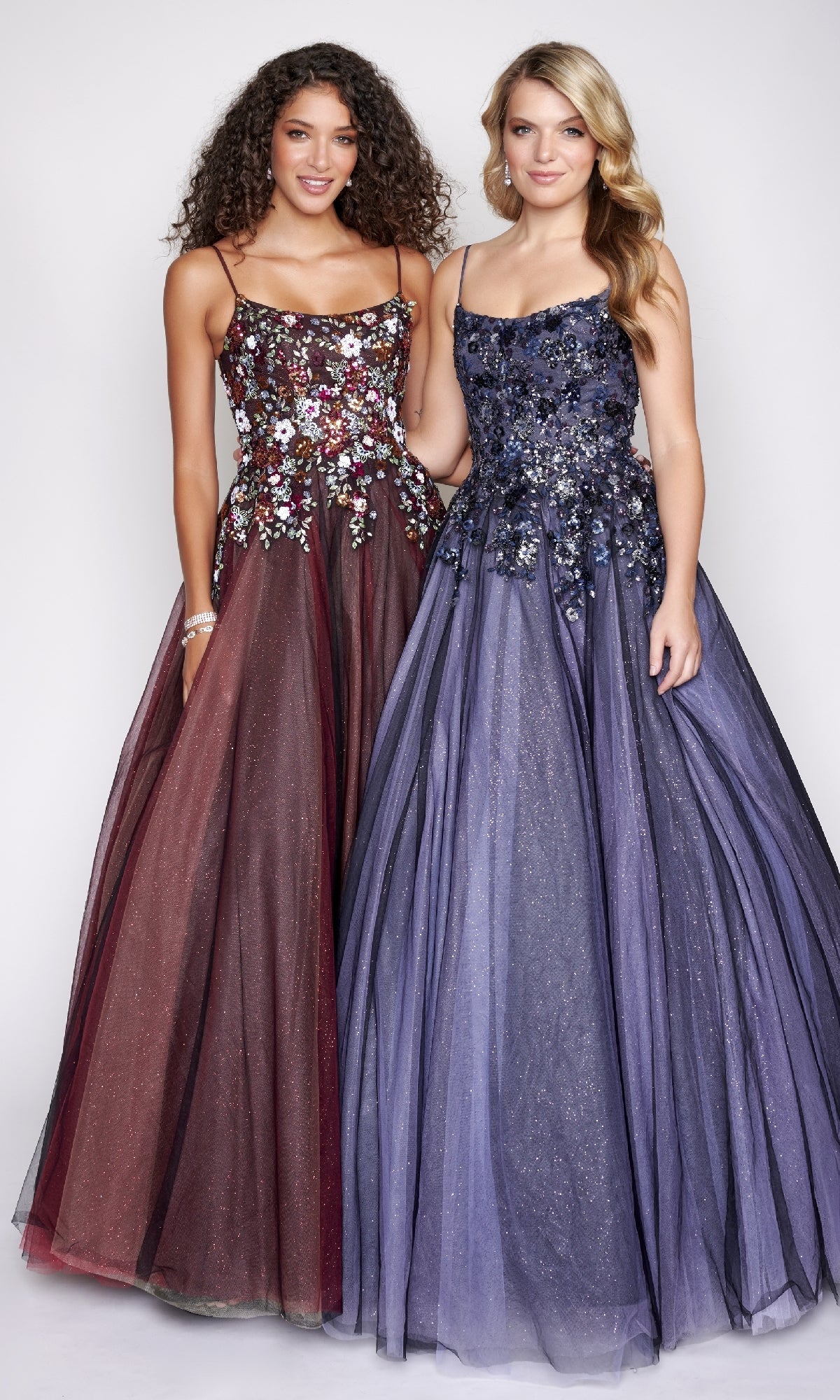 Two women in Nina Canacci 3206 prom ball gowns with floral embellishments and glitter tulle skirts—one burgundy, one deep lavender—stand side by side against a plain light background.