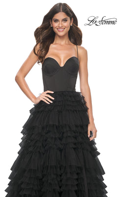 Woman wearing the Lace-Up Ruffle Long Prom Ball Gown: La Femme 32071, featuring a black strapless sweetheart corset bodice and layered ruffled tulle skirt, standing and smiling against a white background with "La Femme" logo.