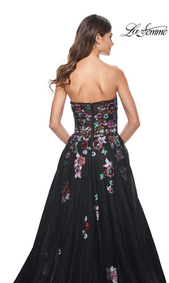 Woman wearing the Le Femme Sequin-Floral Long Black Prom Dress 32072, featuring multicolored sequin floral embroidery and a strapless design, shown from the back with the "La Femme" logo in the top right corner.