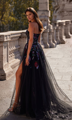 A woman stands outdoors on a stone walkway in the Le Femme Sequin-Floral Long Black Prom Dress 32072, featuring a strapless design, floral details, and a tulle overlay, looking over her shoulder.