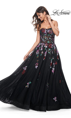 A woman wears the Le Femme Sequin-Floral Long Black Prom Dress 32072, featuring a strapless, sheer-bodice design with floral embroidery and a full tulle skirt. The brand name appears in the top right corner.