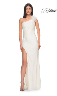 Woman models the La Femme Feathered One-Shoulder Prom Dress 32076—white, long, with a feathered detail and thigh-high slit—against a plain background. "La Femme" designer logo appears in the top right corner.