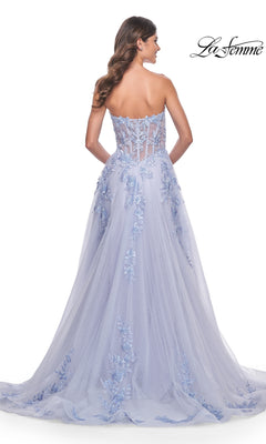 A woman stands with her back to the camera wearing the La Femme Strapless Long A-Line Corset Prom Dress 32082, featuring a sheer corset back, floral embroidery, and a flowing tulle skirt.