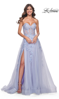 A woman stands smiling in the La Femme Strapless Long A-Line Corset Prom Dress 32082, a floor-length lavender gown with floral lace embroidery, sheer bodice, and high slit.