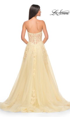 A woman facing away wears the La Femme Strapless Long A-Line Corset Prom Dress 32082 in pale yellow, featuring a sheer floral lace bodice and flowing tulle skirt with train. "La Femme" logo appears in the top right corner.