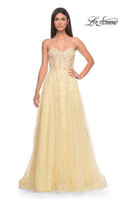 A woman wears the La Femme Strapless Long A-Line Corset Prom Dress 32082 in light yellow, featuring floral lace embroidery and a sheer corset bodice. The La Femme logo appears in the top right corner.