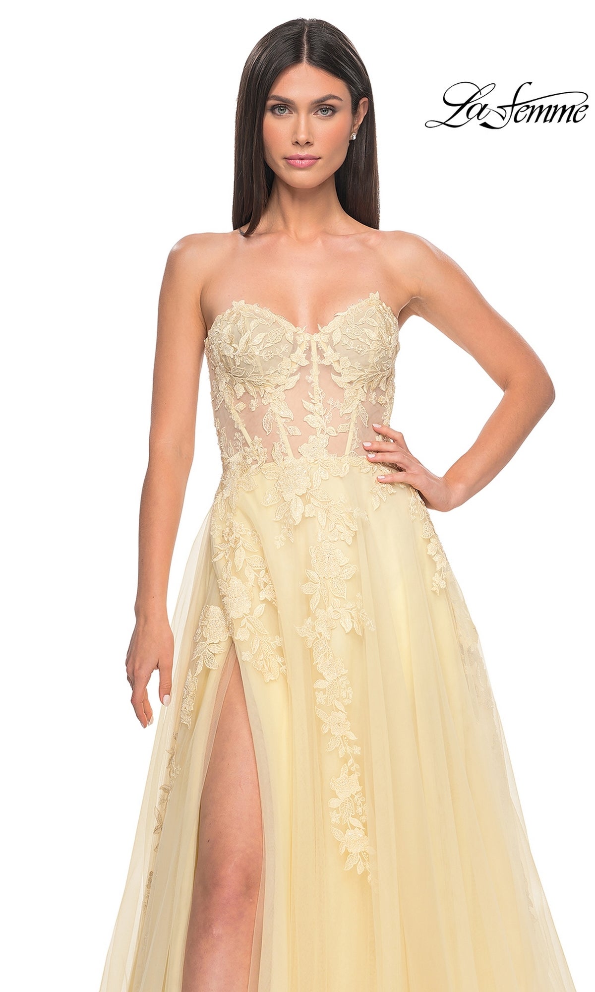 Woman in a light yellow La Femme Strapless Long A-Line Corset Prom Dress 32082 with floral lace applique, sheer bodice, and high slit, posing against a white background. 