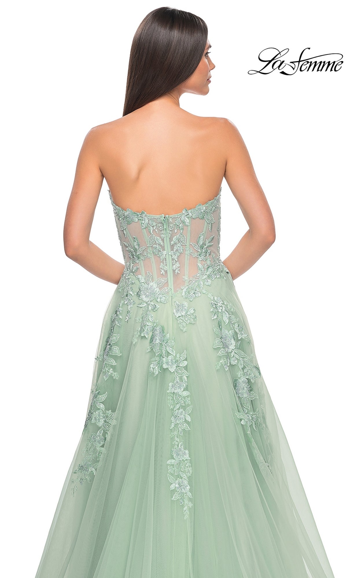 A woman faces away from the camera, wearing the La Femme Strapless Long A-Line Corset Prom Dress 32082 in light green, featuring floral lace embroidery and a sheer back. 