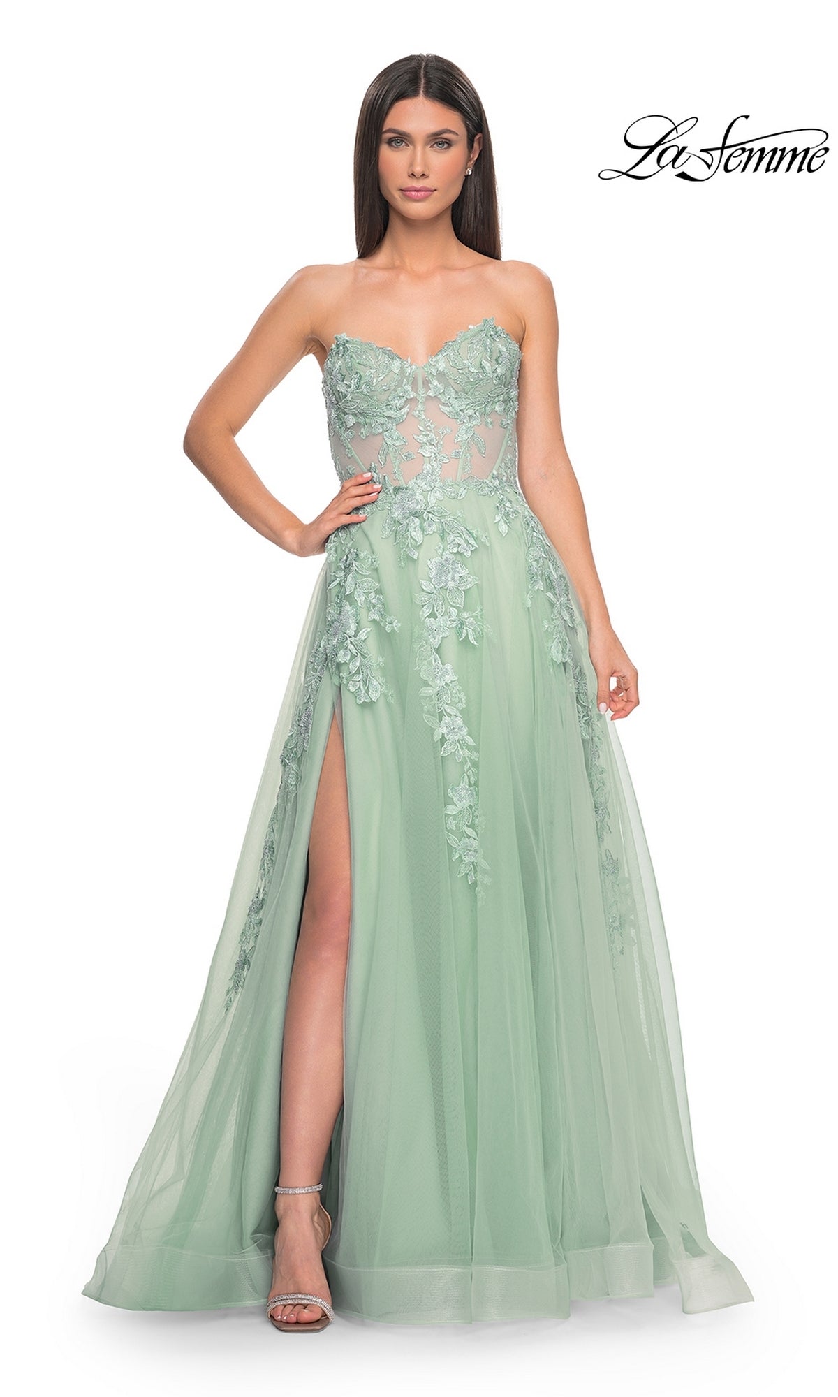A woman poses with one hand on her hip in the La Femme Strapless Long A-Line Corset Prom Dress 32082, mint green with floral lace embroidery, a sheer bodice, and a high slit, set against a white background.
