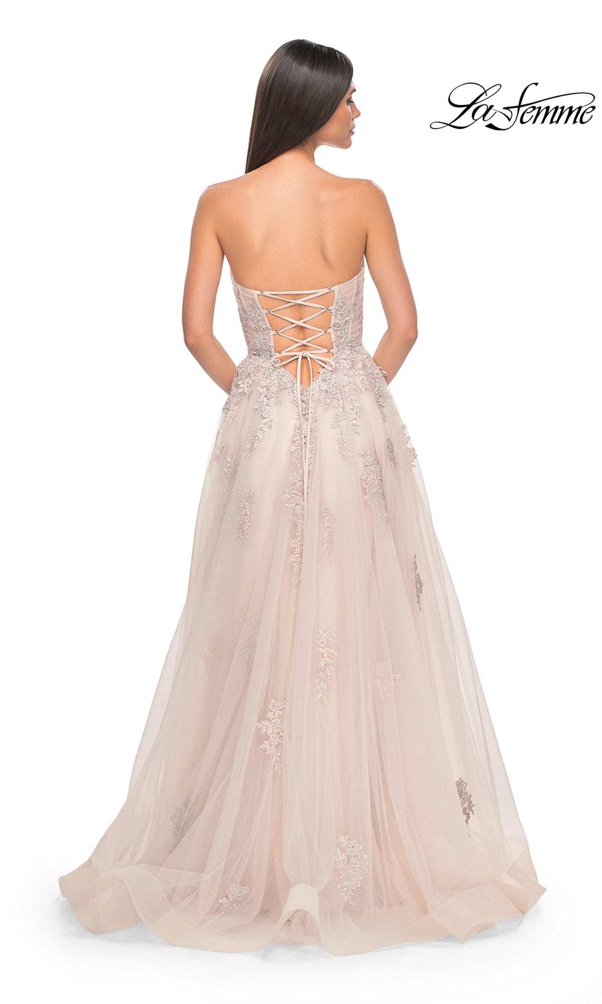 A woman with her back to the camera models the La Femme Backless Strapless Long Prom Dress 32084, a blush floor-length A-line gown featuring a lace-up back and floral embroidery.
