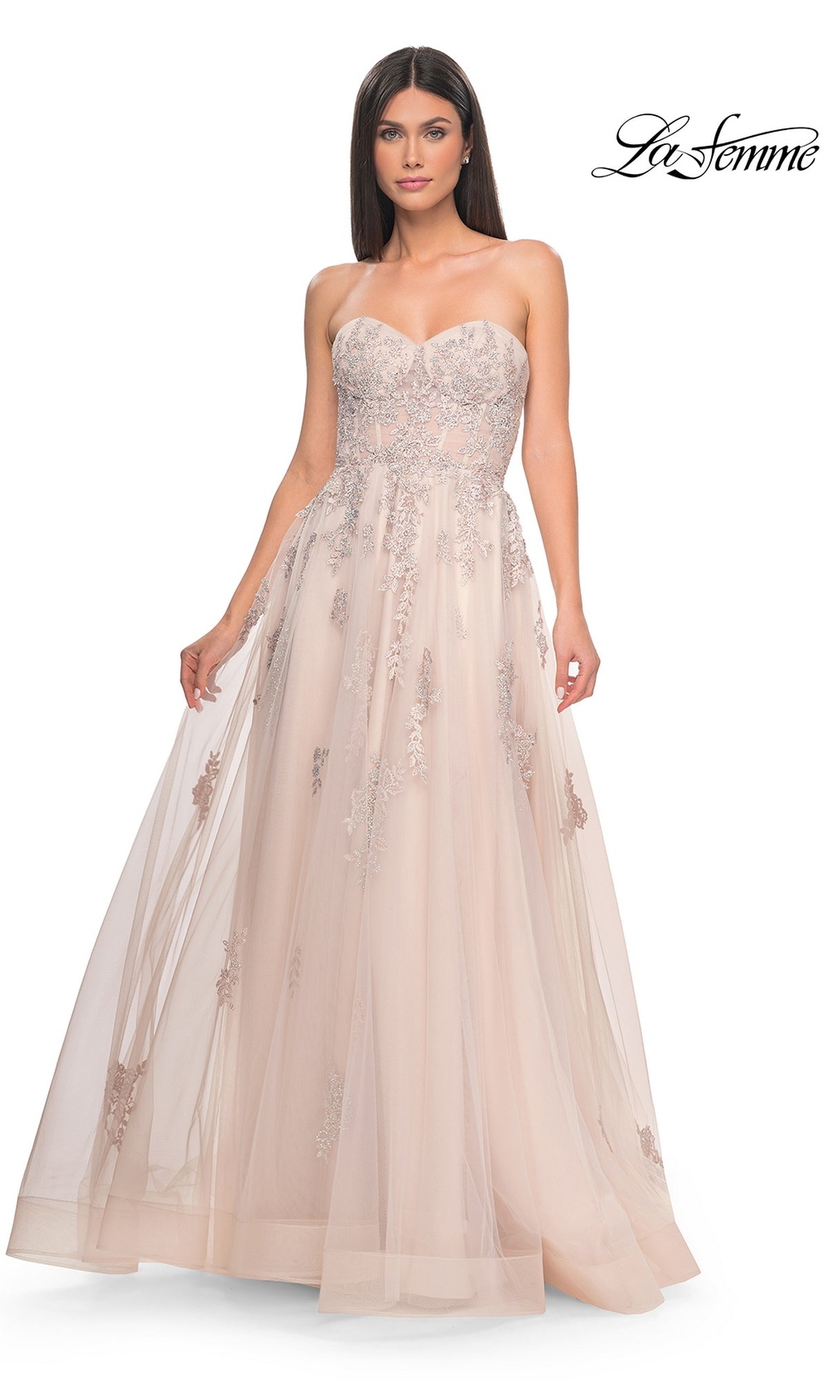 A woman wears the La Femme Backless Strapless Long Prom Dress 32084 in blush pink, featuring silver floral embroidery and a flowing tulle skirt for an enchanting formal look.