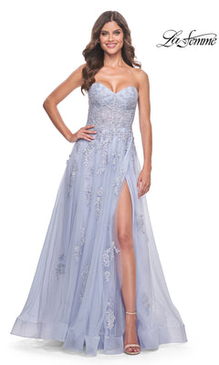 A woman stands smiling in the La Femme Backless Strapless Long Prom Dress 32084, a light periwinkle A-line gown featuring floral embroidery and a thigh-high slit.