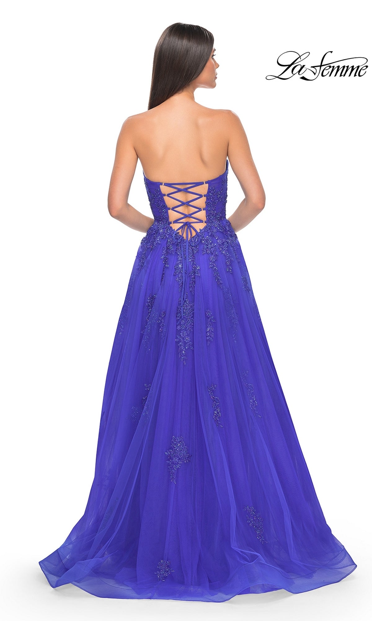 A woman with long brown hair models the La Femme Backless Strapless Long Prom Dress 32084 in royal blue, featuring a floor-length a-line silhouette, lace-up back, and beaded details, standing with her back to the camera.