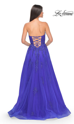 A woman with long brown hair models the La Femme Backless Strapless Long Prom Dress 32084 in royal blue, featuring a floor-length a-line silhouette, lace-up back, and beaded details, standing with her back to the camera.