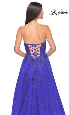 Woman wearing the La Femme Backless Strapless Long Prom Dress 32084 in royal blue, featuring embroidered lace and a lace-up corset back, facing away from the camera. The La Femme logo appears in the top right corner.