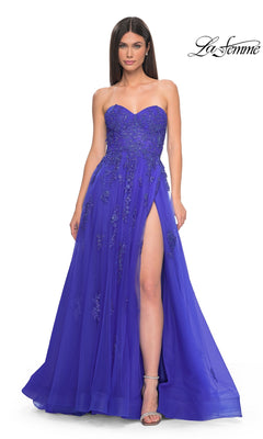 A woman models the La Femme Backless Strapless Long Prom Dress 32084, a royal blue A-line gown with floral embellishments, sweetheart neckline, and high slit, posing elegantly against a white background.