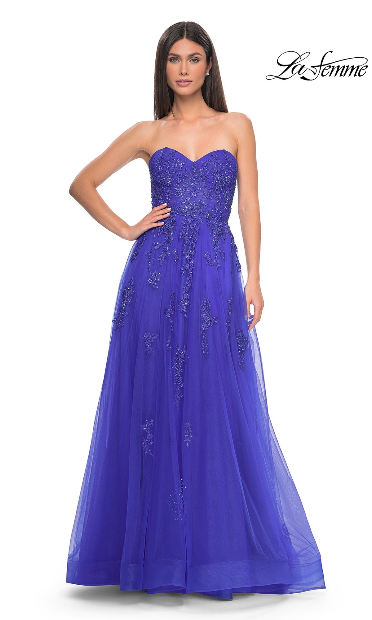 A woman poses in the La Femme Backless Strapless Long Prom Dress 32084, a floor-length royal blue gown with beaded floral embellishments and a fitted bodice.