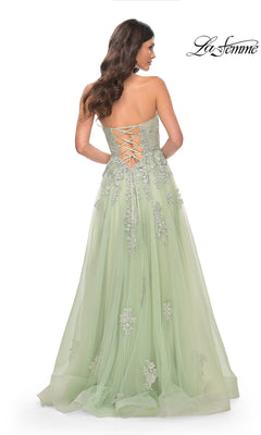 A woman models the La Femme Backless Strapless Long Prom Dress 32084 in light green, featuring floral embellishments, a lace-up back, and an a-line silhouette. The La Femme logo is displayed in the top right corner.