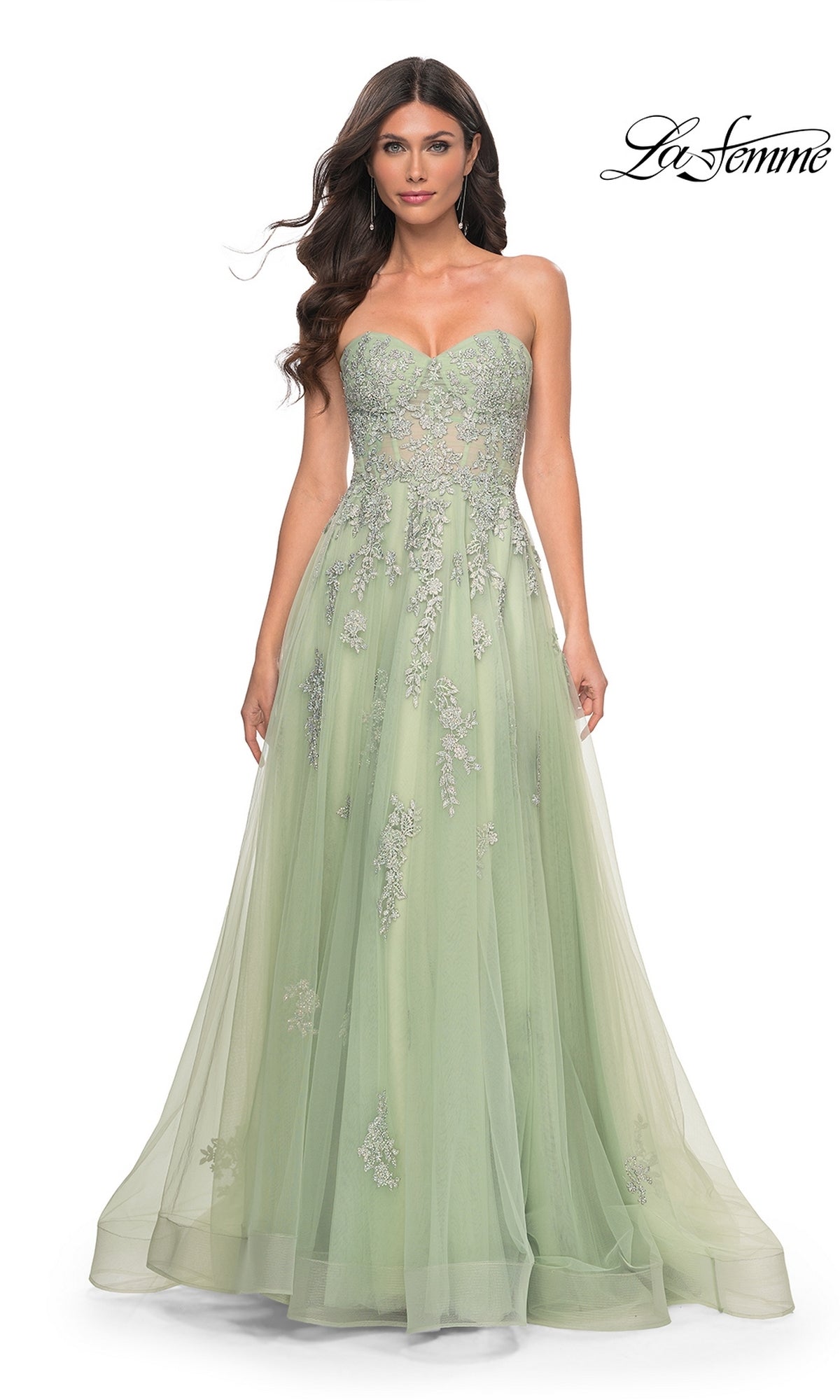 A woman wears the La Femme Backless Strapless Long Prom Dress 32084, a light green A-line gown with an embellished tulle skirt and floral details, posing against a white background.