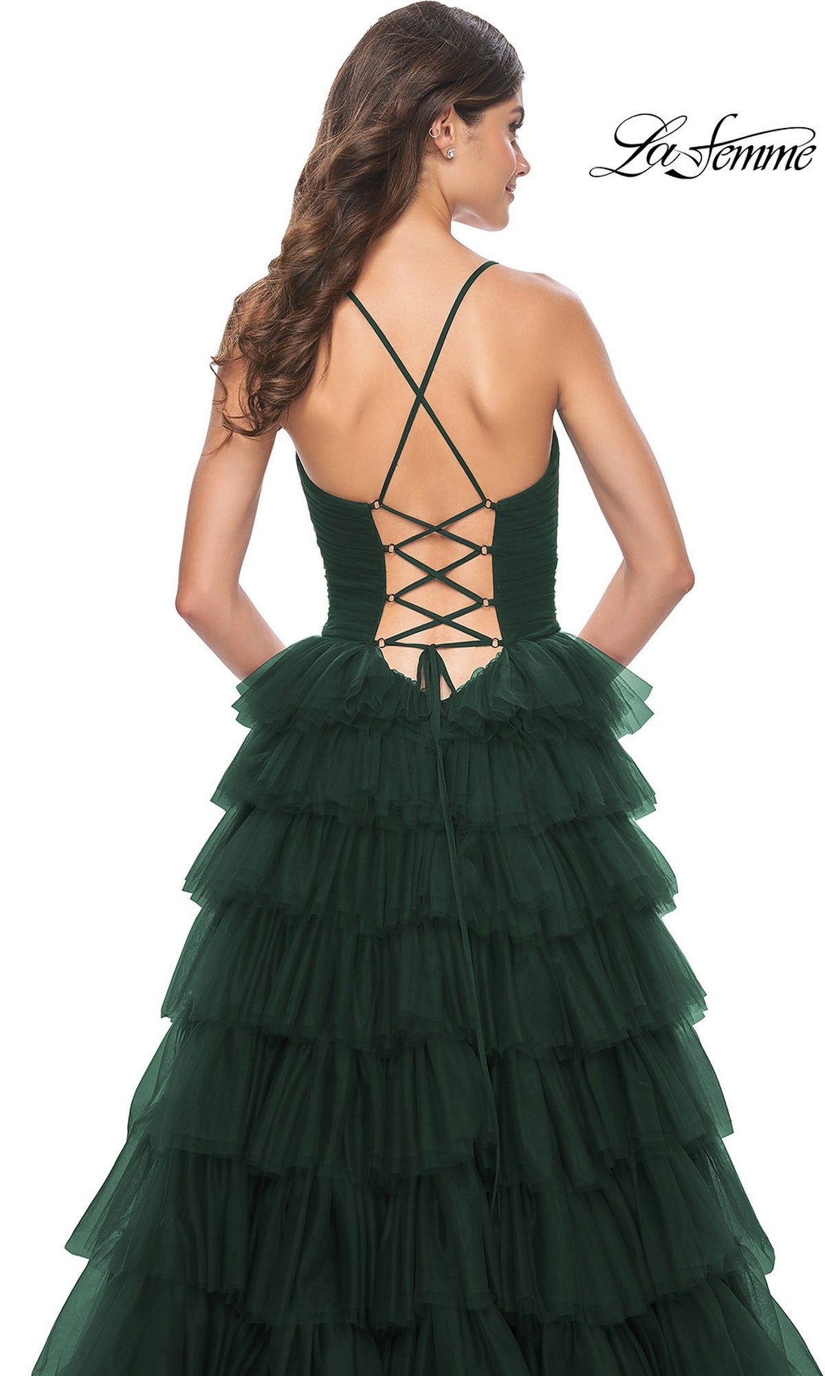 A woman wearing the La Femme Lace-Up Long Tiered Prom Dress 32086 in dark green, featuring a lace-up back and thin crisscross straps, stands against a white background.