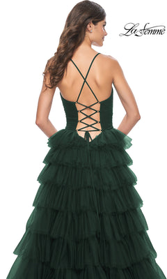 A woman wearing the La Femme Lace-Up Long Tiered Prom Dress 32086 in dark green, featuring a lace-up back and thin crisscross straps, stands against a white background.