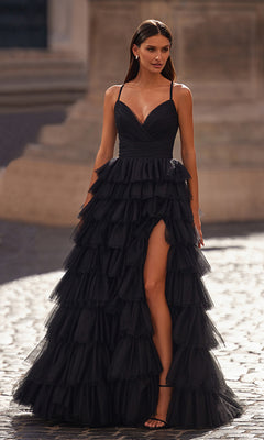 A woman wearing the La Femme Lace-Up Long Tiered Prom Dress 32086 in black, featuring spaghetti straps, a high slit, and tiered ruffles, stands outdoors on a cobblestone surface.