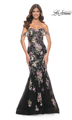 Woman smiling in the La Femme Long Floral Mermaid Prom Dress 32087, a black off-the-shoulder gown with floral embroidery. "La Femme" logo appears in the top right corner.
