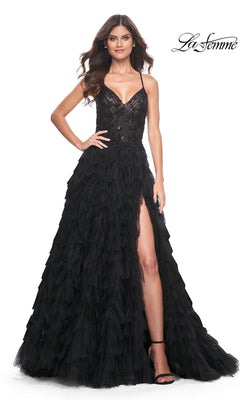 A woman poses elegantly with one hand on her hip in the La Femme Long Black Ruffled Prom Ball Gown 32108, featuring spaghetti straps and a high slit, against a white background.