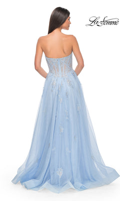 A woman with long brown hair is shown from the back, wearing the La Femme Strapless Long A-Line Prom Dress 32111 in light blue, featuring a sheer embellished bodice with embroidered-lace appliques and a flowing tulle skirt.