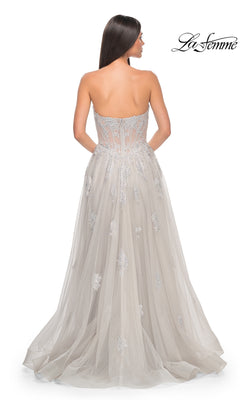 A woman stands facing away in the La Femme Strapless Long A-Line Prom Dress 32111, featuring silver embroidered-lace appliques, a sheer back, visible boning, and a flowing tulle skirt.