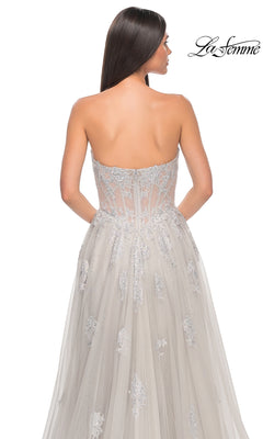 A woman with long brown hair models the La Femme Strapless Long A-Line Prom Dress 32111 in light gray, featuring embroidered-lace appliques and tulle, shown from the back with the La Femme logo in the top right corner.