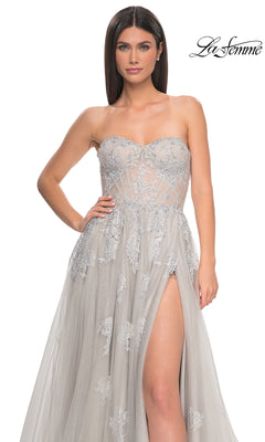 A woman models the La Femme Strapless Long A-Line Prom Dress 32111 in light gray, featuring embroidered lace appliques and a high slit; "La Femme" logo appears in the top right corner.